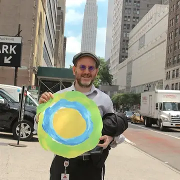 A man holding the Idealist logo poses in the street.