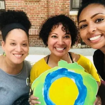 Three women smiling with the Idealist logo between them.