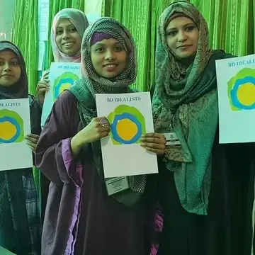 A group of women with head coverings hold up papers with the Idealist logo on it.