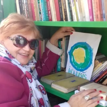 A woman stands next to a bookshelf holding up a picture with the Idealist logo on it.