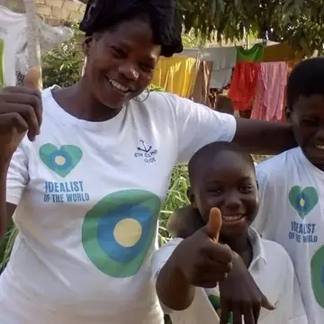 Three people with Idealist shirts stand with their thumbs up.