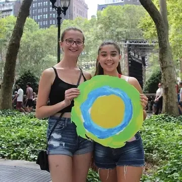 Two young ladies pose in the park with the Idealist logo.