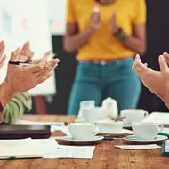 Group of co-workers applauding someone during a meeting, coffee cups strewn across the table.