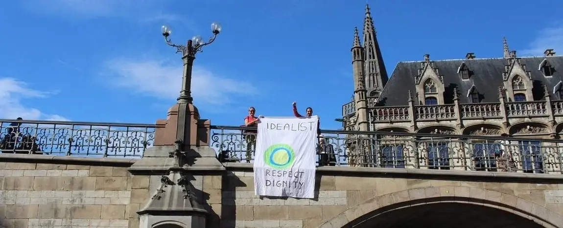 Two idealists hold a banner with the Idealist logo on it over a bridge.